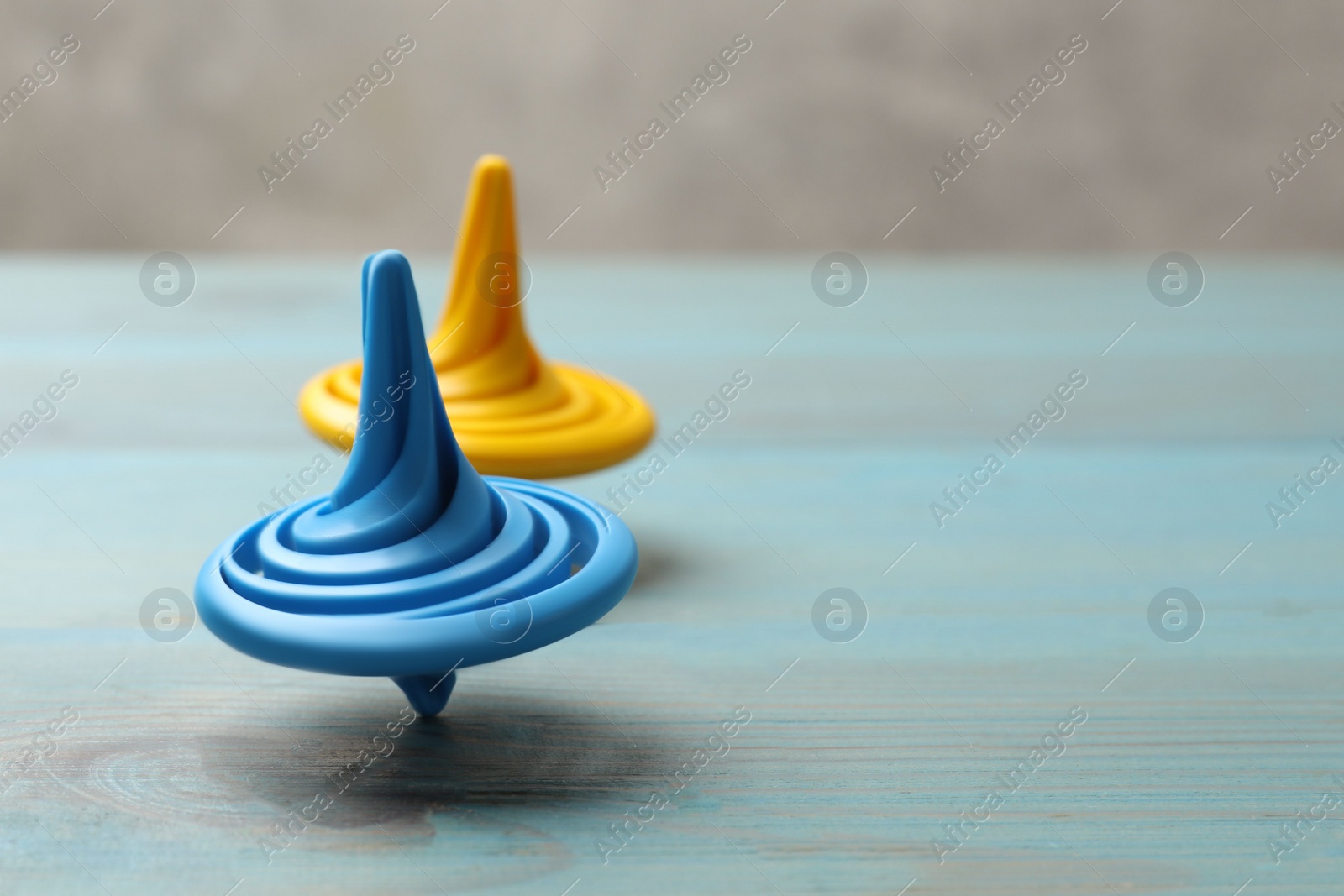 Photo of Bright spinning tops on light blue wooden table, closeup. Space for text