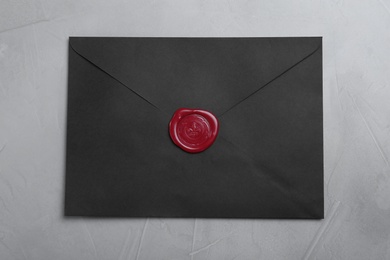 Photo of Black envelope with wax seal on grey background, top view