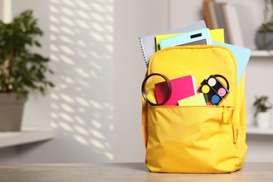 Photo of Yellow backpack with different school stationery on table indoors, space for text