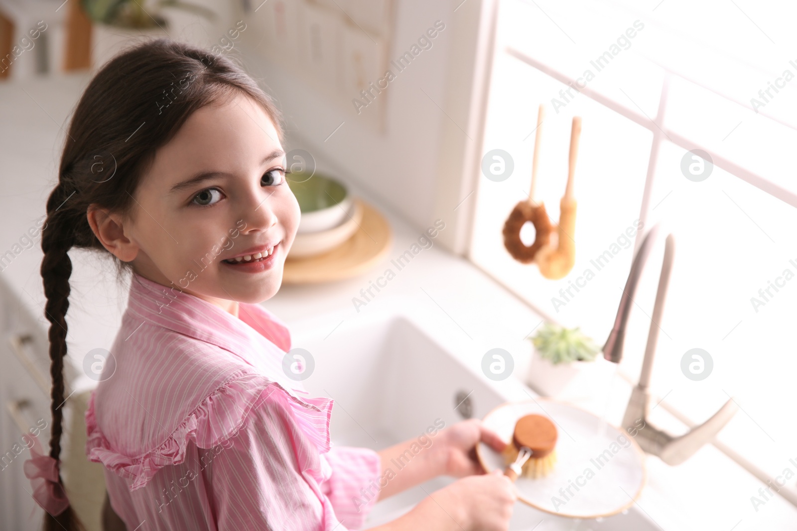 Photo of Little girl washing dishes in kitchen at home