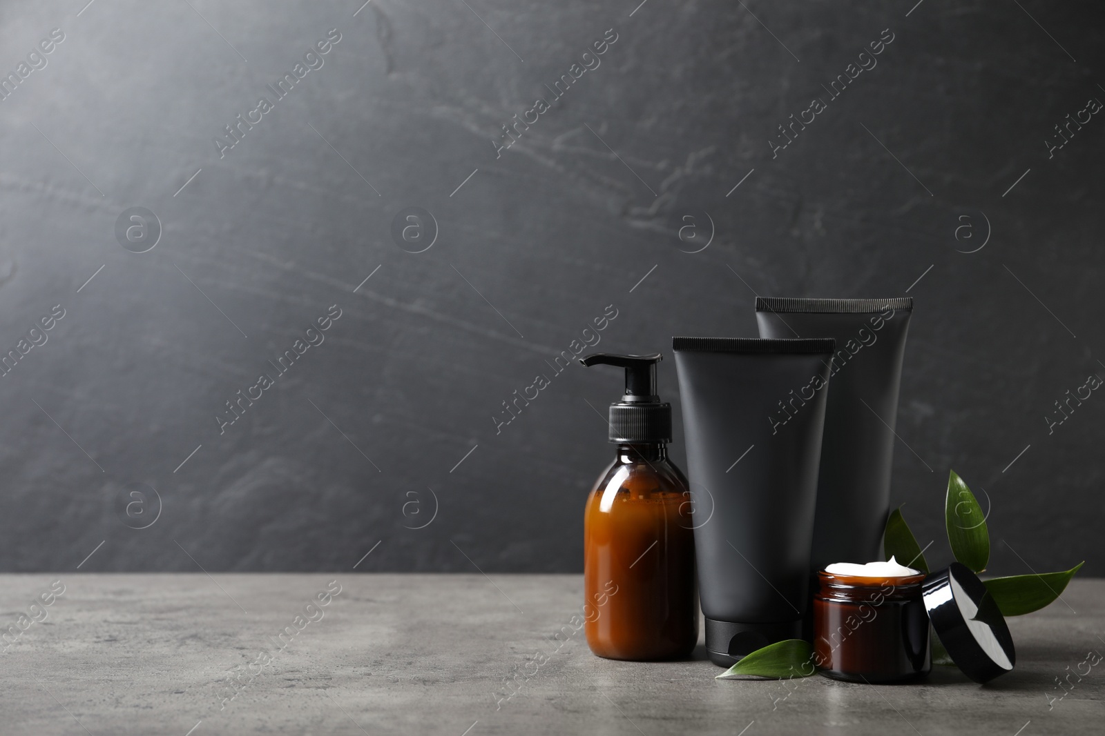 Photo of Facial cream and other men's cosmetic with green leaves on grey stone table. Mockup for design