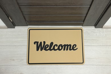 Photo of Beige doormat with word Welcome on white floor near entrance, top view