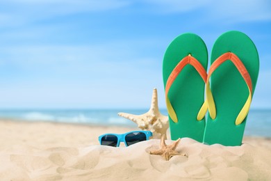 Green flip flops, starfishes and sunglasses on sandy beach near sea 