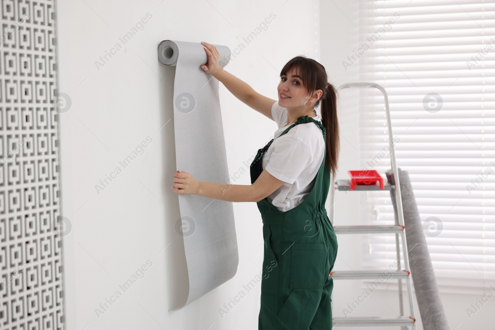 Photo of Woman hanging stylish gray wallpaper in room