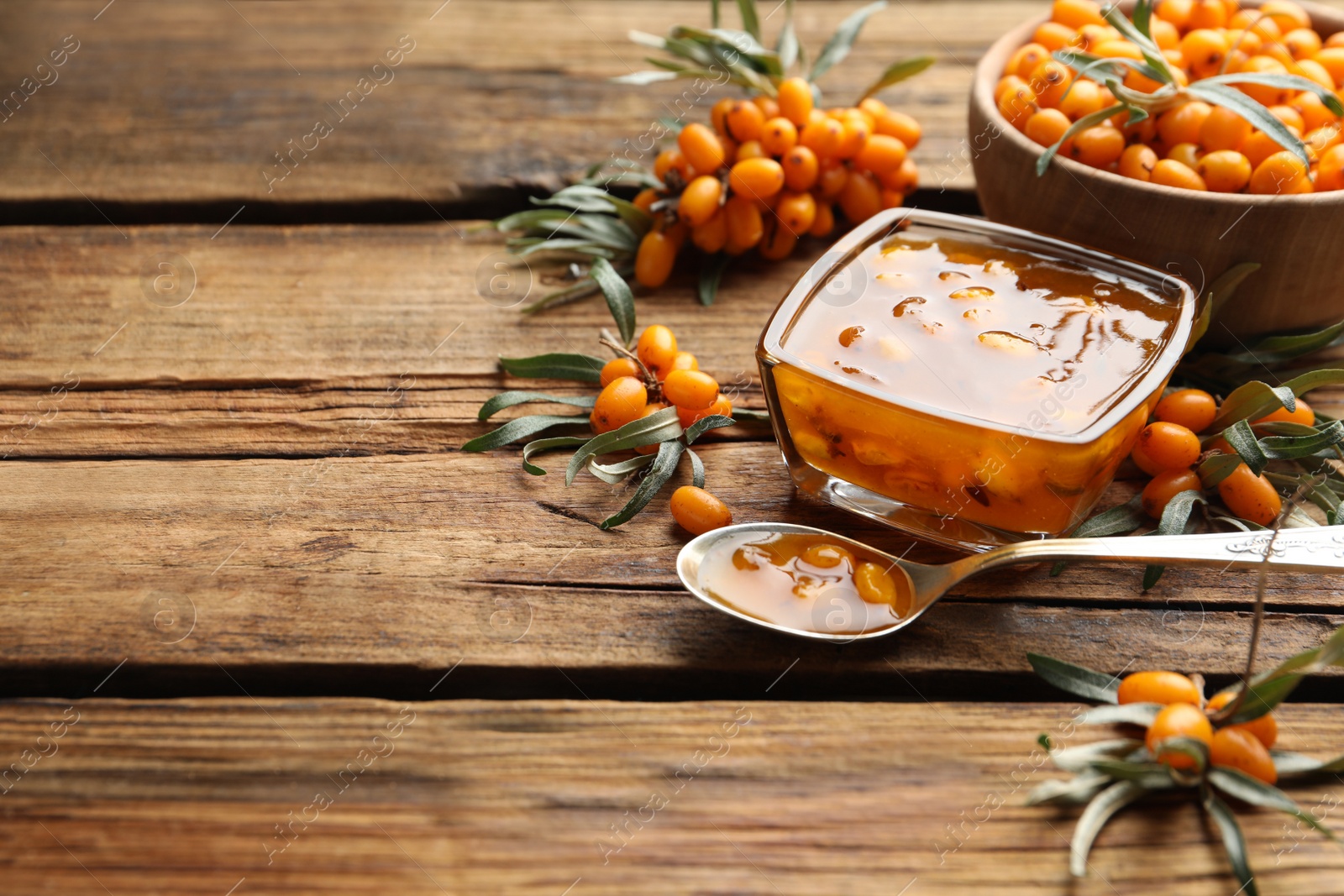 Photo of Delicious sea buckthorn jam and fresh berries on wooden table. Space for text