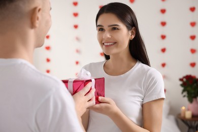 Photo of Young woman receiving gift from her boyfriend indoors. Valentine`s day celebration