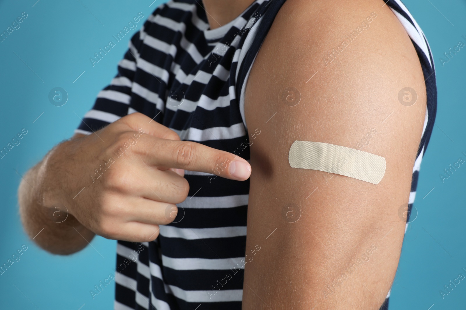 Photo of Vaccinated man showing medical plaster on his arm against light blue background, closeup