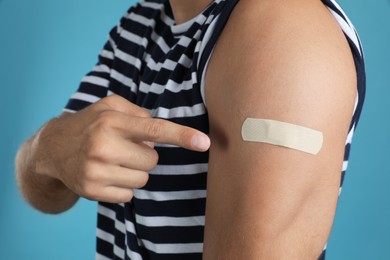 Photo of Vaccinated man showing medical plaster on his arm against light blue background, closeup