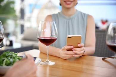 Photo of Young woman with smartphone and glass of wine at table