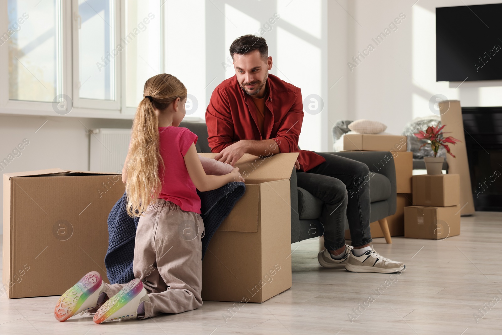 Photo of Family settling into home. Happy father and daughter unpacking boxes in new apartment. Moving day