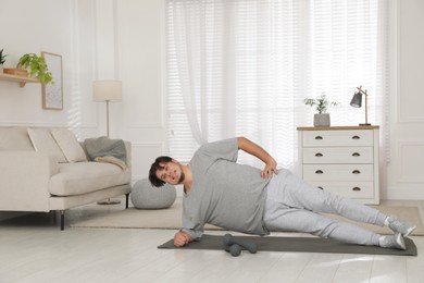 Overweight man doing side plank exercise on mat at home
