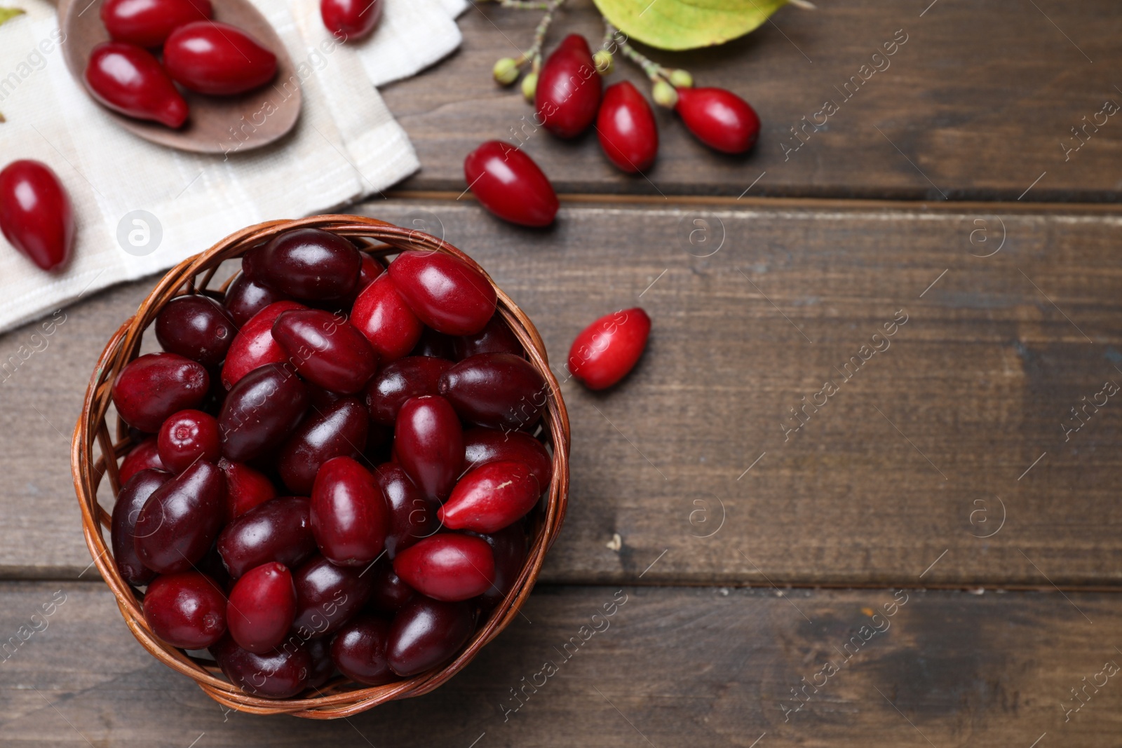 Photo of Fresh ripe dogwood berries with wicker bowl on wooden table, flat lay. Space for text