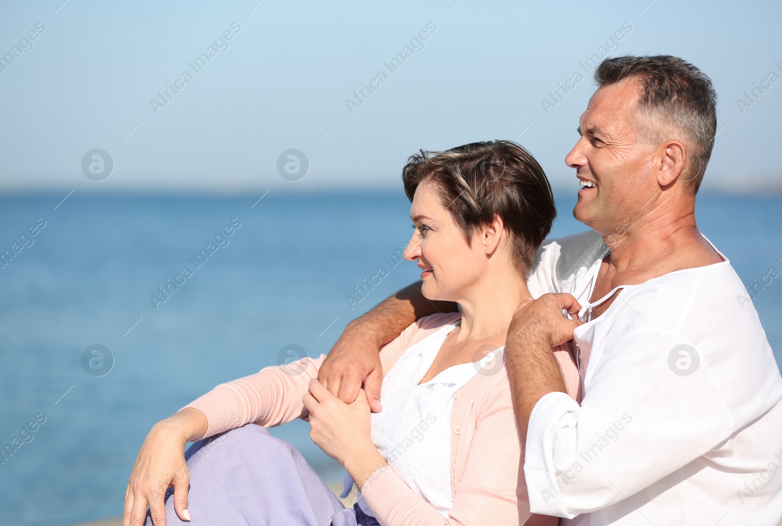 Photo of Happy mature couple sitting together at beach on sunny day