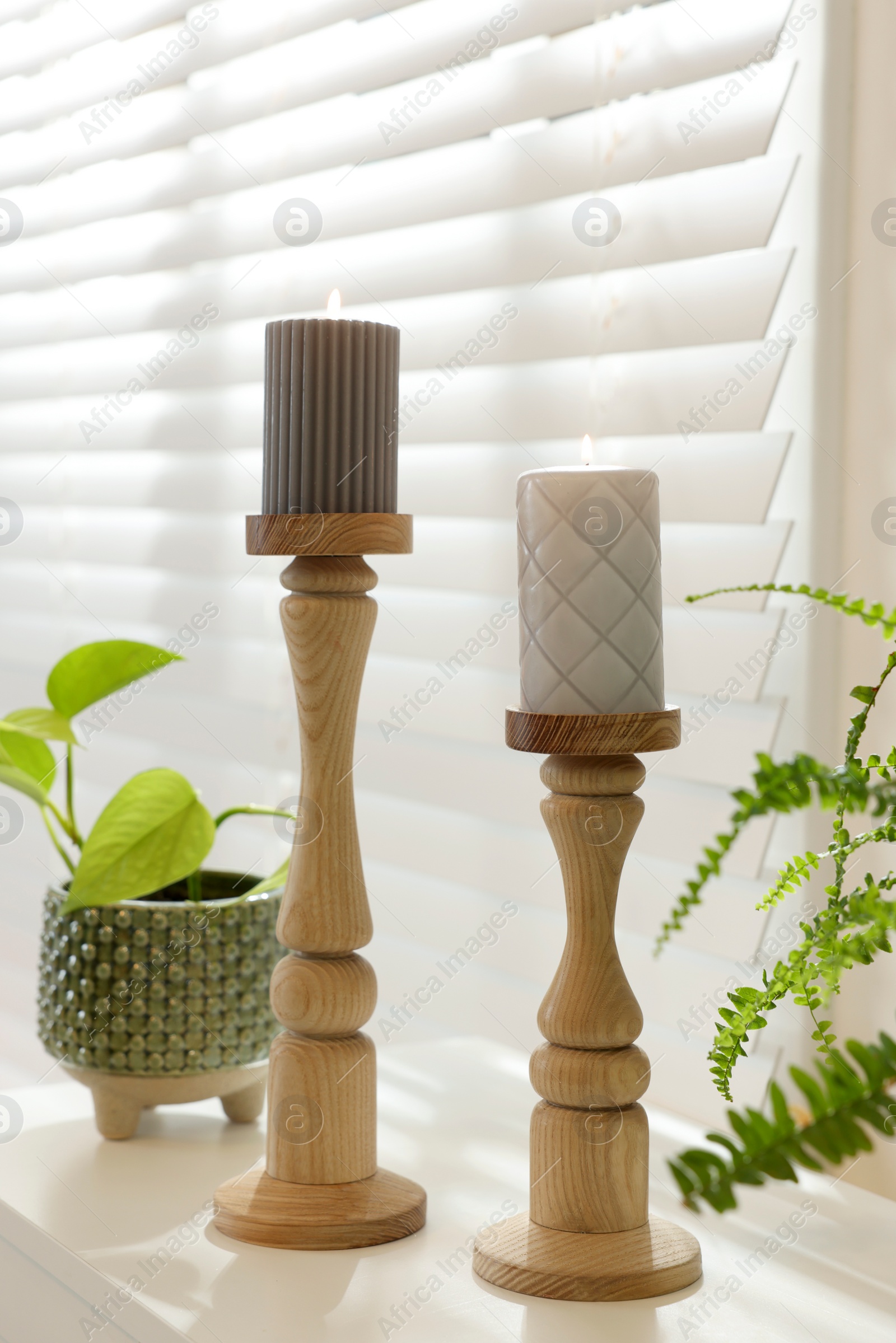 Photo of Pair of beautiful wooden candlesticks and houseplants on white table in room