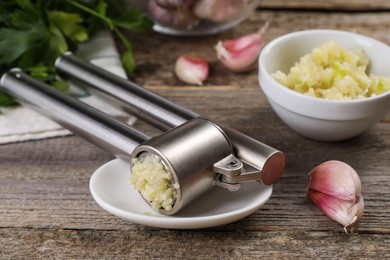 Photo of Garlic press, cloves and mince on wooden table, closeup