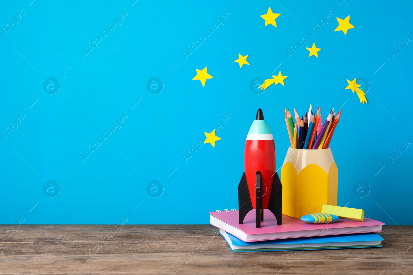 Photo of Bright toy rocket and school supplies on wooden desk. Space for text