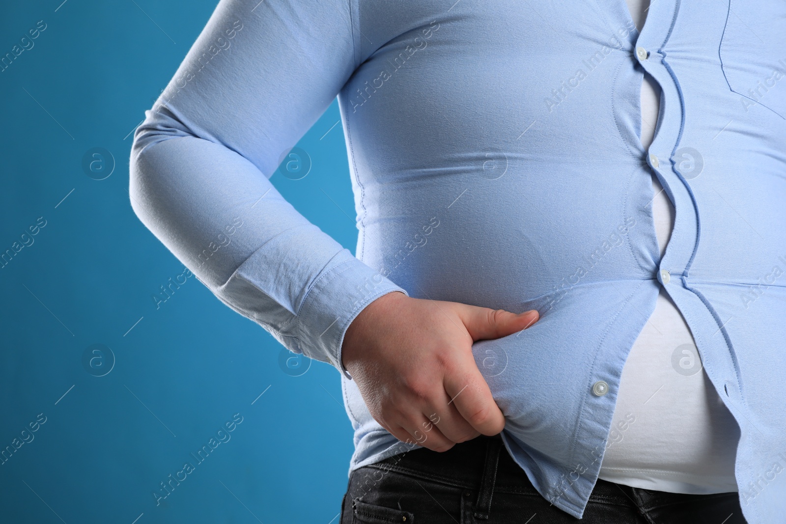 Photo of Overweight man in tight shirt on light blue background, closeup