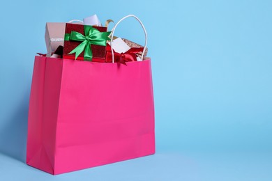 Photo of Pink paper shopping bag full of gift boxes on light blue background. Space for text