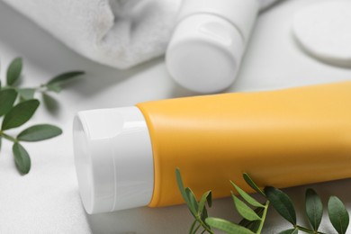 Tube of face cleansing product and green leaves on white table, closeup