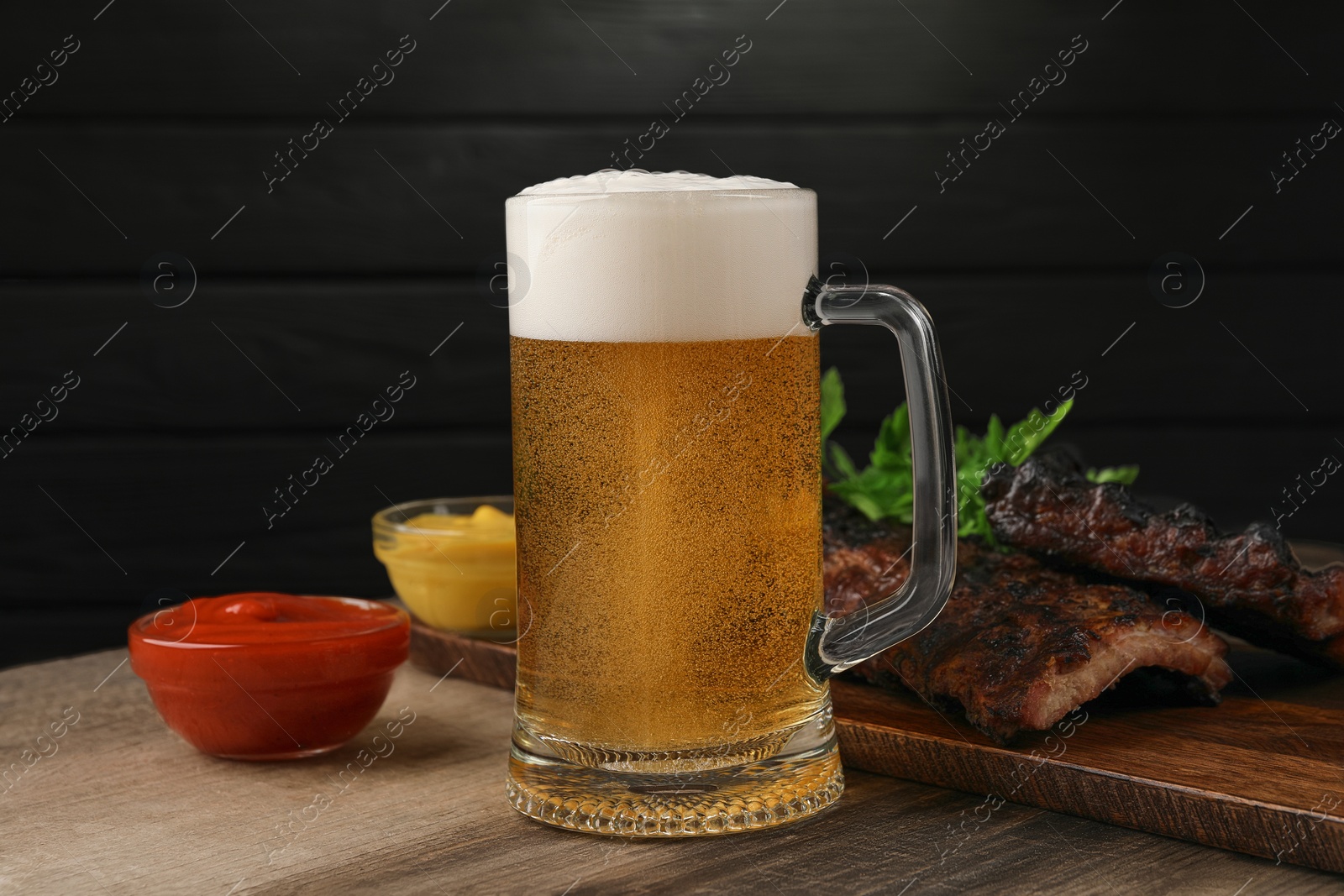 Photo of Mug with beer, delicious grilled ribs and sauces on wooden table