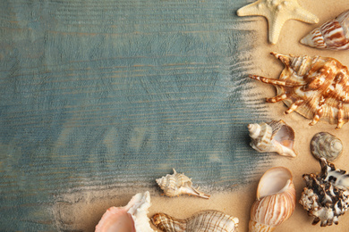 Different sea shells and sand on light blue wooden table, flat lay. Space for text