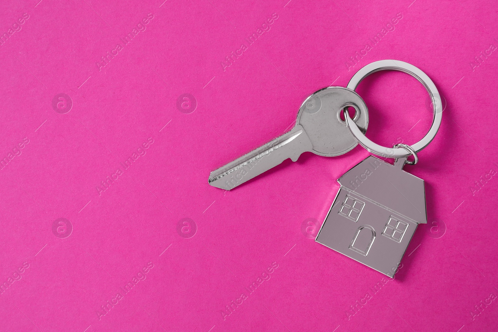 Photo of Key with keychain in shape of house on pink background, top view. Space for text