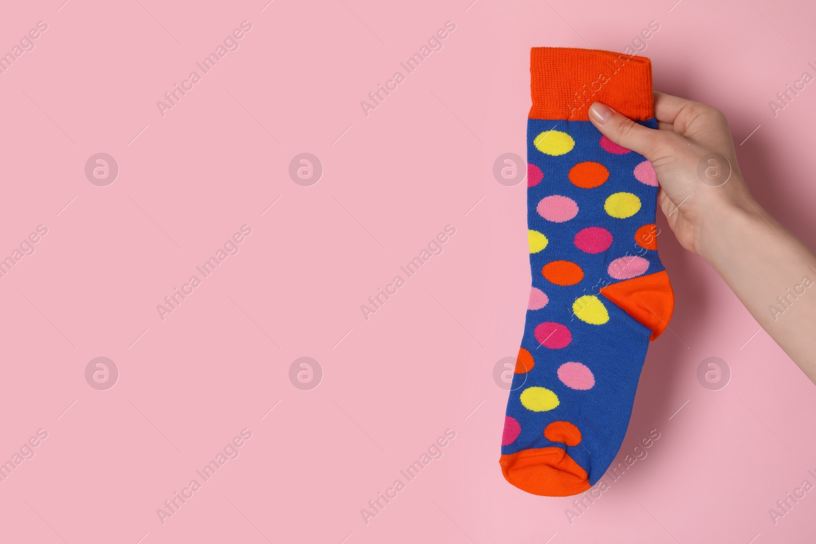 Photo of Woman holding colorful sock on light pink background, closeup. Space for text