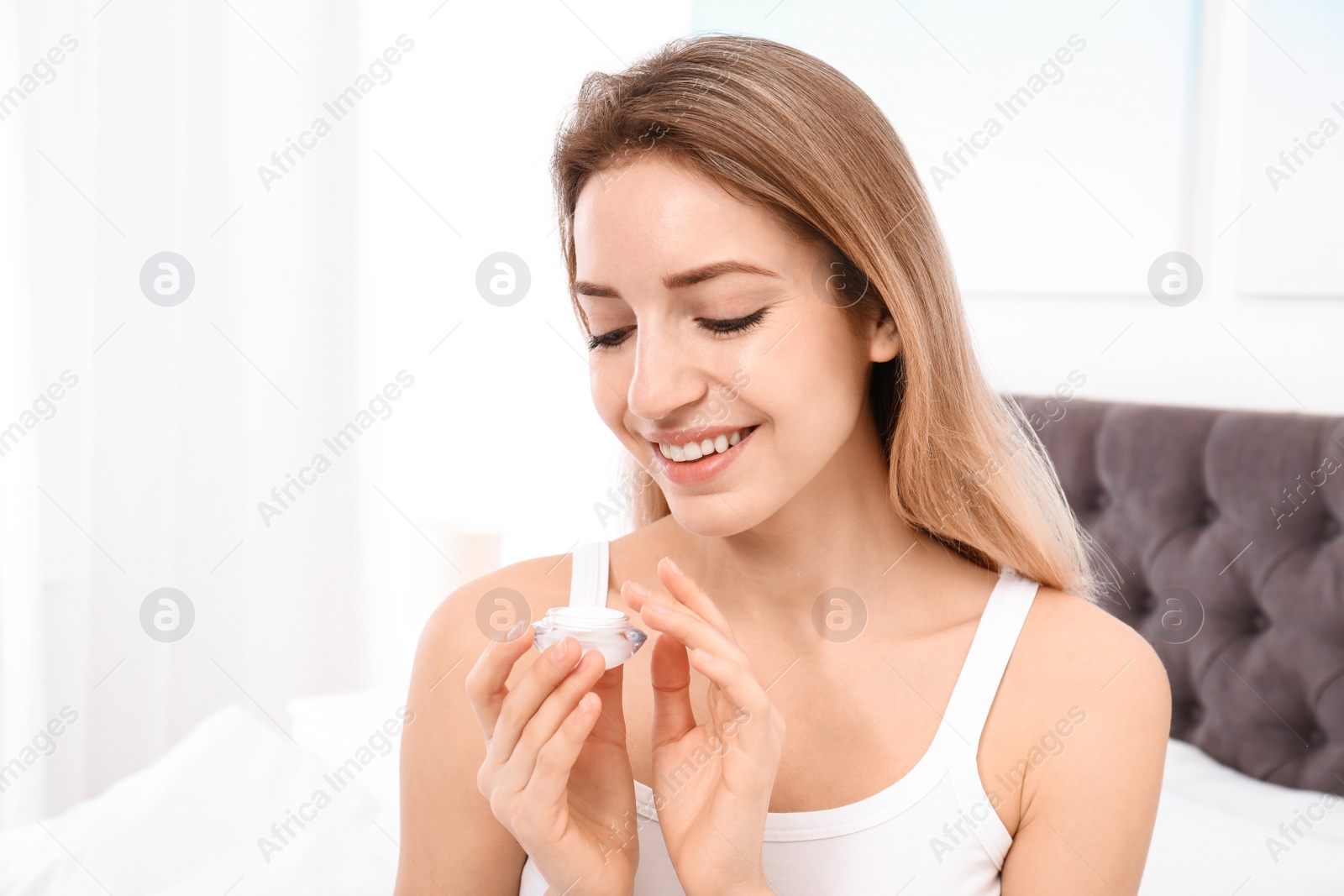 Photo of Portrait of young woman with jar of cream indoors. Beauty and body care