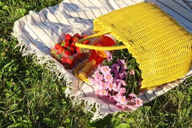 Yellow wicker bag with beautiful flowers, bottle of wine and strawberries on picnic blanket outdoors