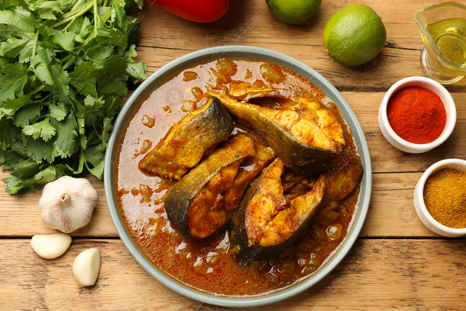 Photo of Tasty fish curry and ingredients on wooden table, flat lay. Indian cuisine