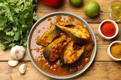 Photo of Tasty fish curry and ingredients on wooden table, flat lay. Indian cuisine