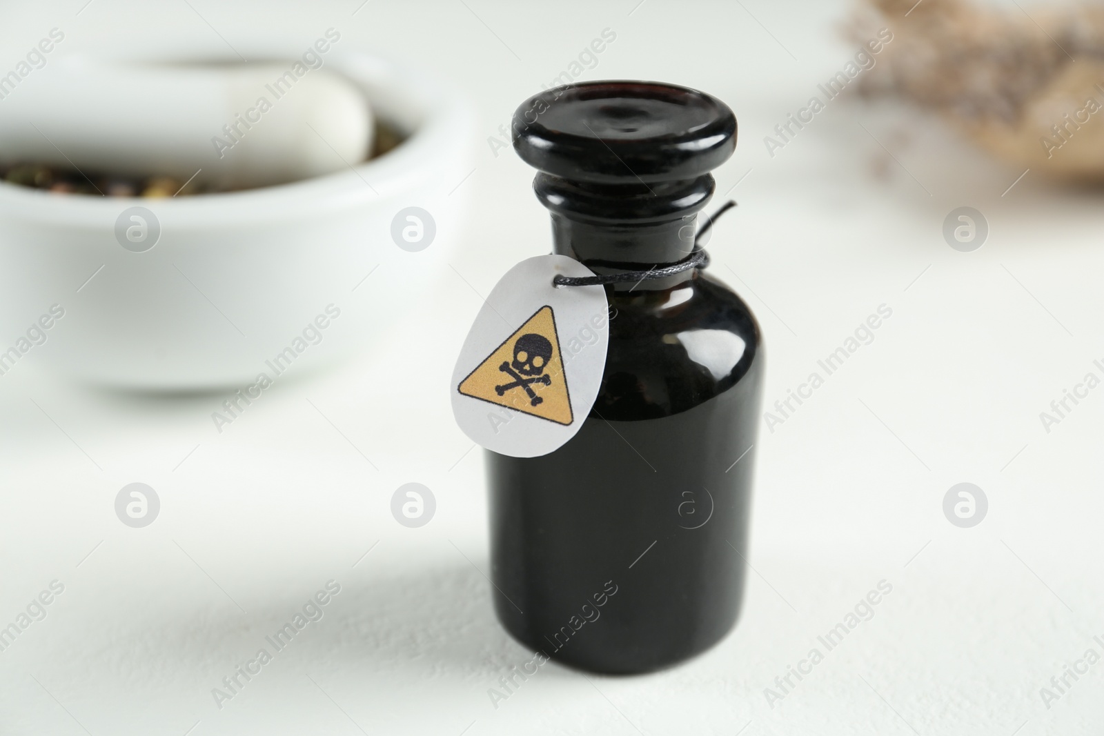 Photo of Glass bottle of poison with warning sign on light background, closeup