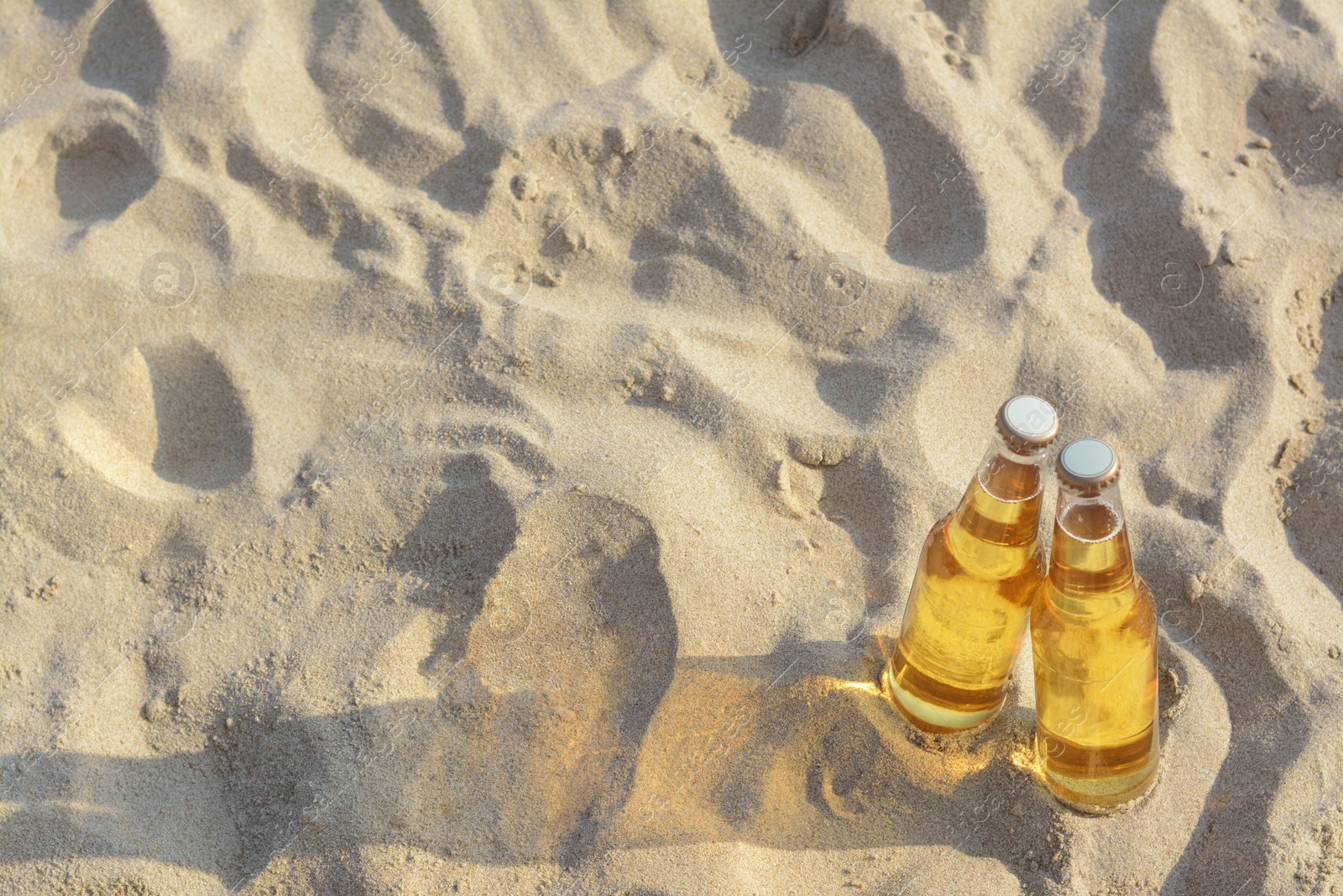 Photo of Bottles of cold beer on sandy beach, above view. Space for text