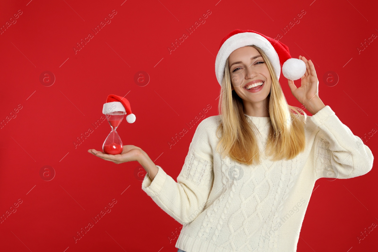 Photo of Woman in Santa hat with hourglass on red background. Christmas countdown