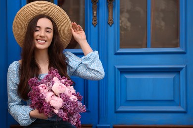 Photo of Beautiful woman with bouquet of spring flowers near blue wooden doors, space for text