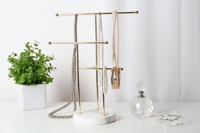 Photo of Interior element. Holder with set of luxurious jewelry, perfume and plant on white dressing table