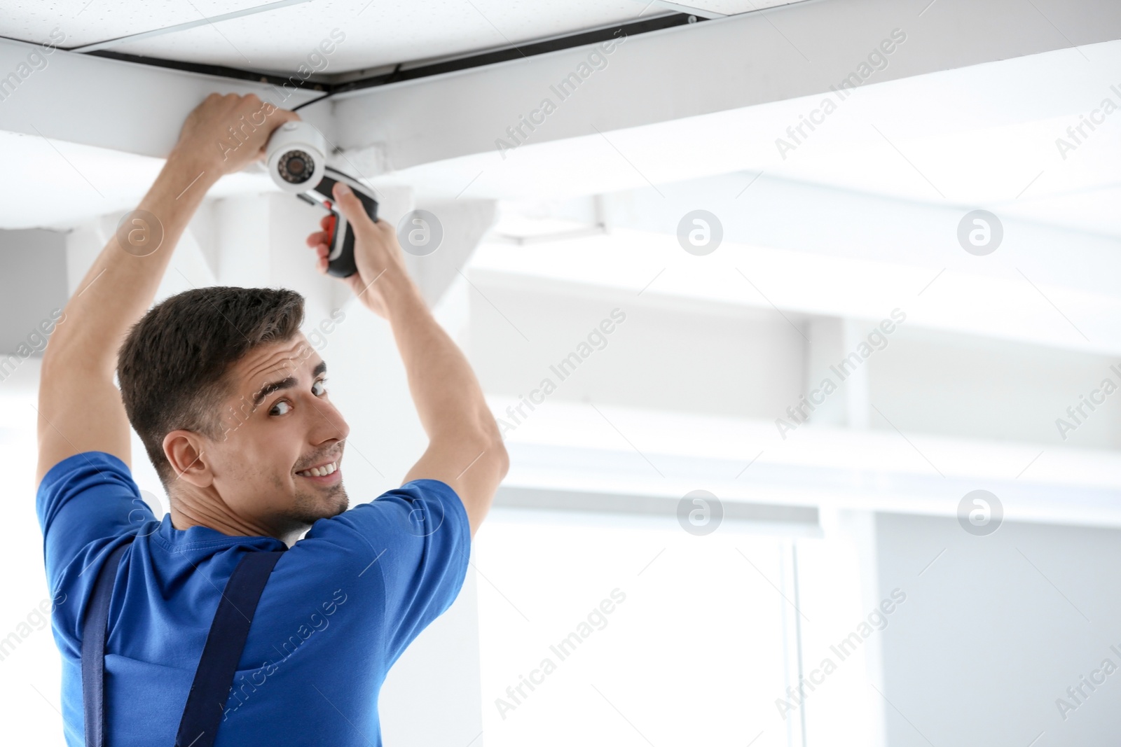 Photo of Technician installing CCTV camera on ceiling indoors