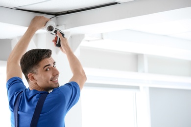 Technician installing CCTV camera on ceiling indoors