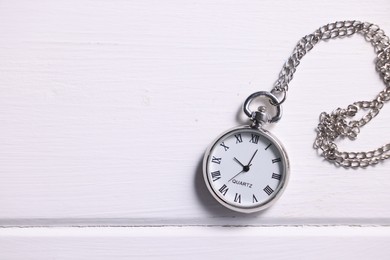Silver pocket clock with chain on white wooden table, top view. Space for text