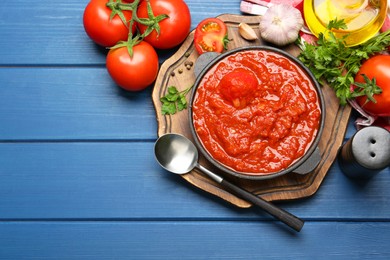 Photo of Homemade tomato sauce in bowl, spoon and ingredients on blue wooden table, flat lay. Space for text