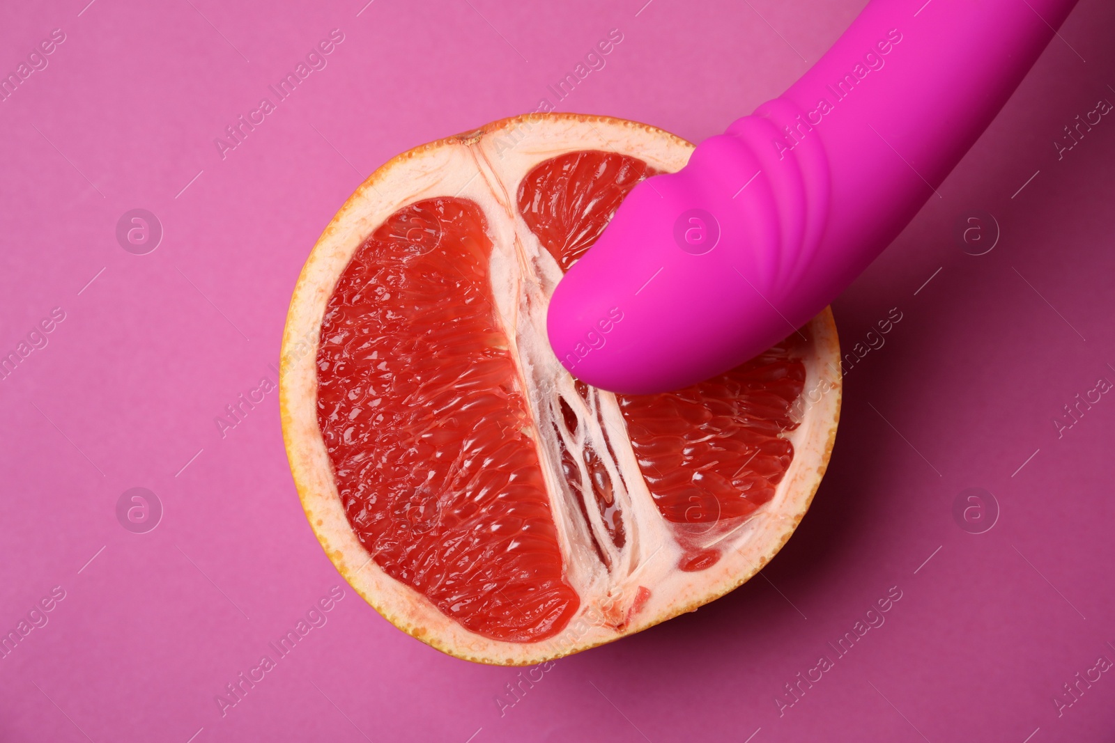 Photo of Half of grapefruit and vibrator on purple background, flat lay. Sex concept
