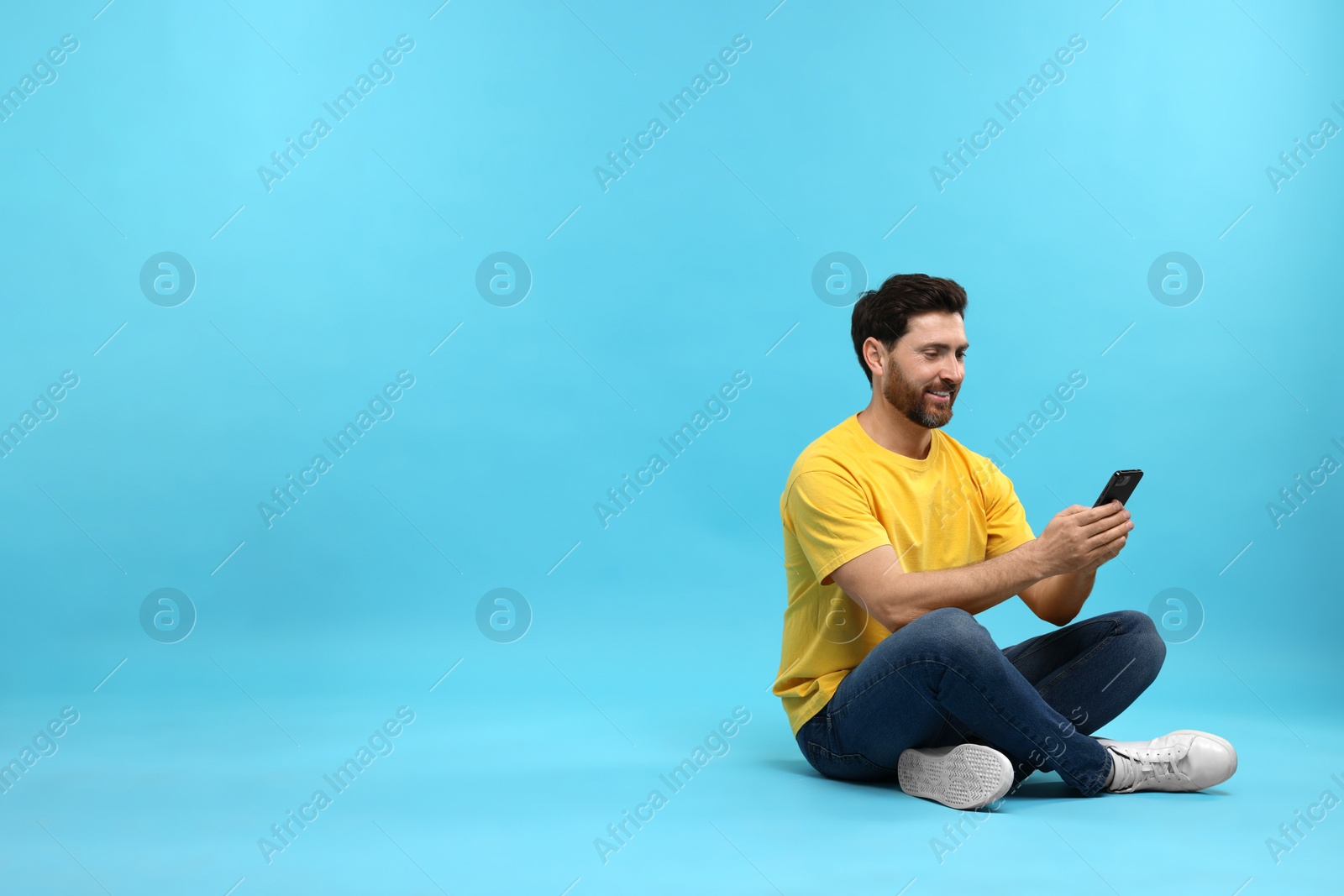 Photo of Smiling man with smartphone on light blue background. Space for text