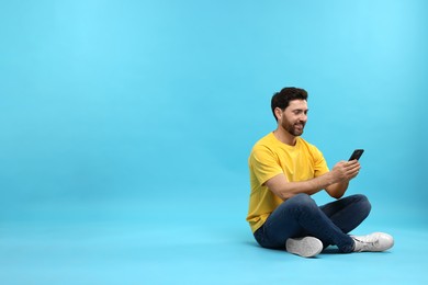 Smiling man with smartphone on light blue background. Space for text