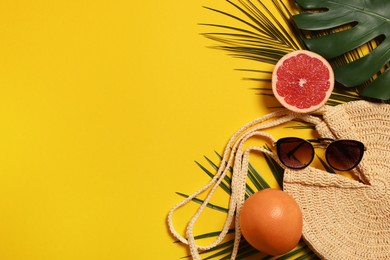 Beach bag, sunglasses, grapefruits and leaves on orange background, flat lay. Space for text