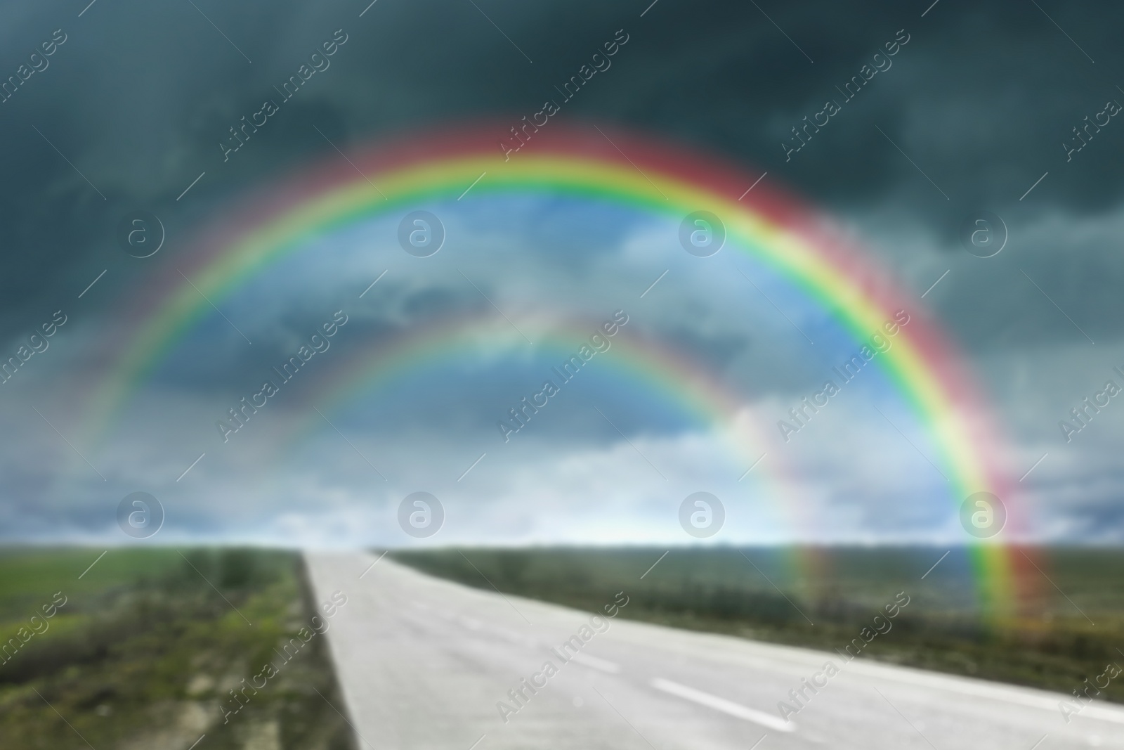 Image of Amazing double rainbow over country road under stormy sky, blurred view