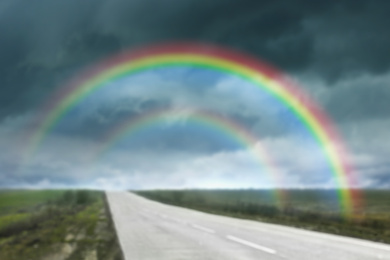 Image of Amazing double rainbow over country road under stormy sky, blurred view