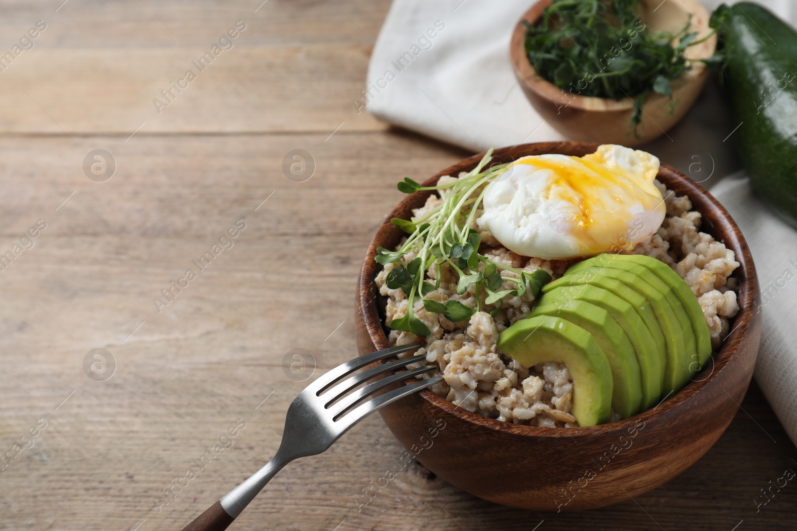 Photo of Delicious boiled oatmeal with poached egg, avocado and fork on wooden table, space for text