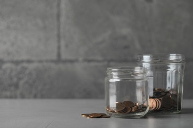 Photo of Glass jars with coins on grey table. Space for text