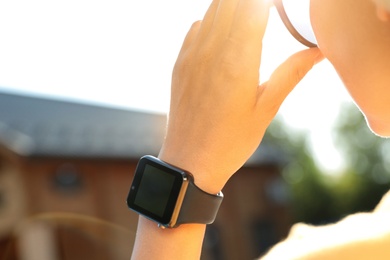 Photo of Woman wearing modern smart watch outdoors, closeup