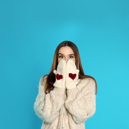 Photo of Beautiful young woman in mittens and white sweater on blue background. Winter season